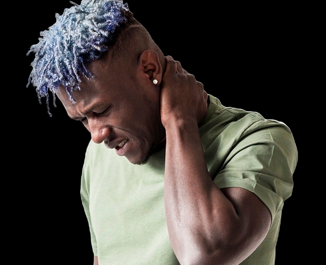 Junger Mann mit blauen Haaren und Schmerzensgesicht fasst sich an den Nacken.